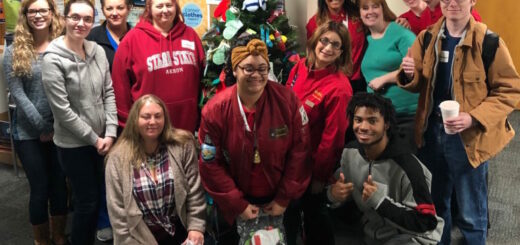 crowd of Phi Theta Kappans surrounding a pine tree adorned with cloth mittens.