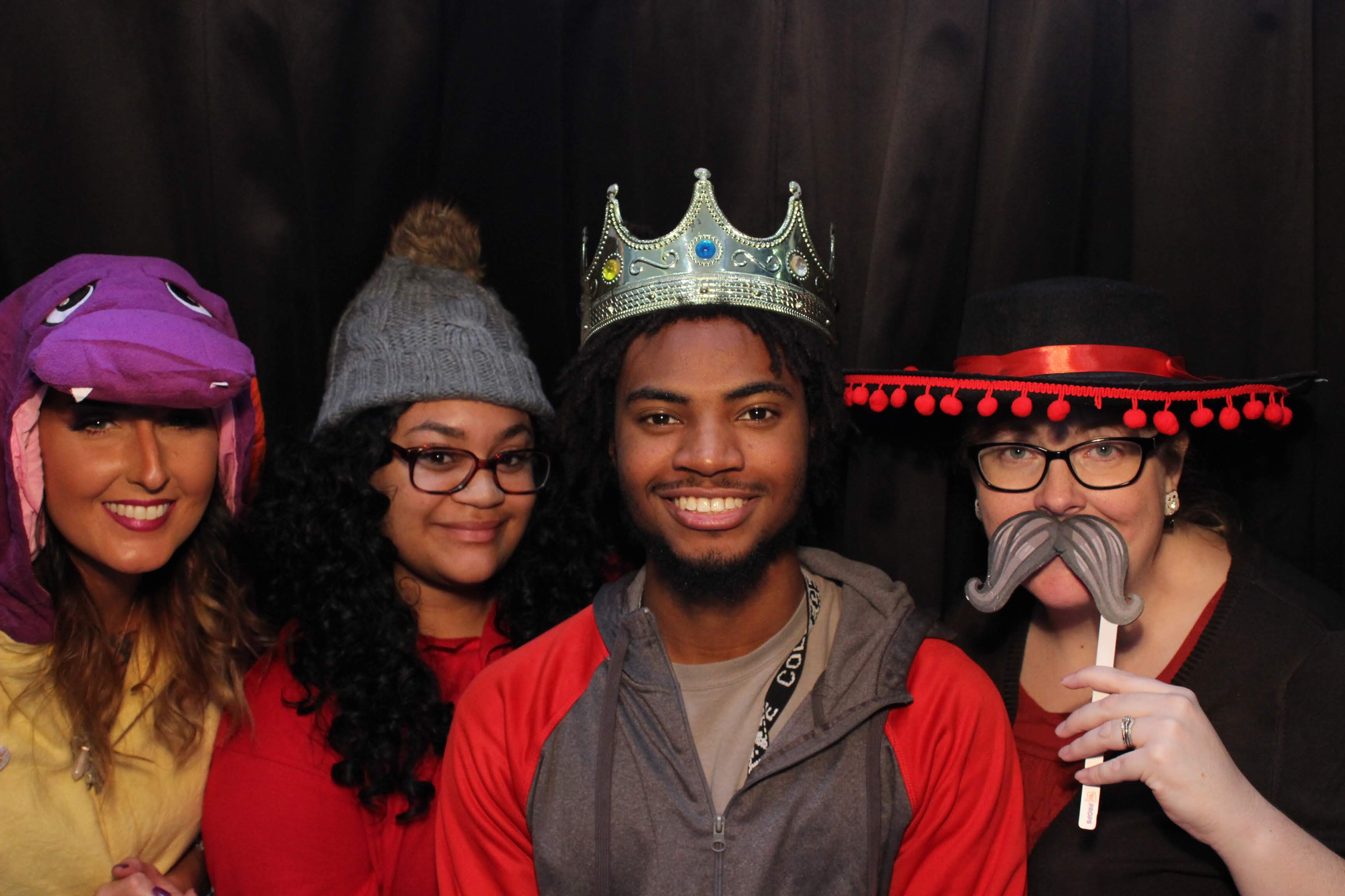 Four Phi Theta Kappans having fun in a photo booth, wearing various props.