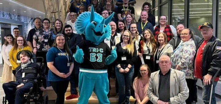 crowd of Phi Theta Kappans posing for a photo with a blue triceratops mascot.