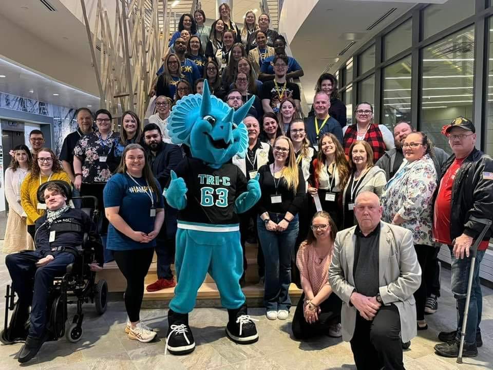 crowd of Phi Theta Kappans posing for a photo with a blue triceratops mascot.