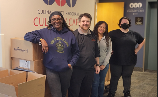 Four Phi Theta Kappans standing in front of a cart of boxed books.