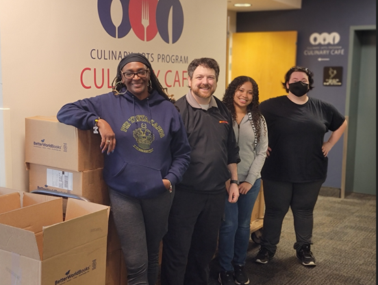 Four Phi Theta Kappans standing in front of a cart of boxed books.