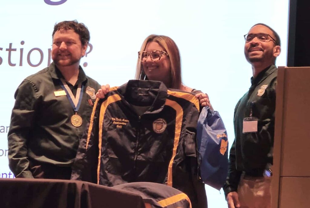 Two regional officers smiling proudly on either side of the headquarters representative as they hold their newly acquired Ohio Region jacket.