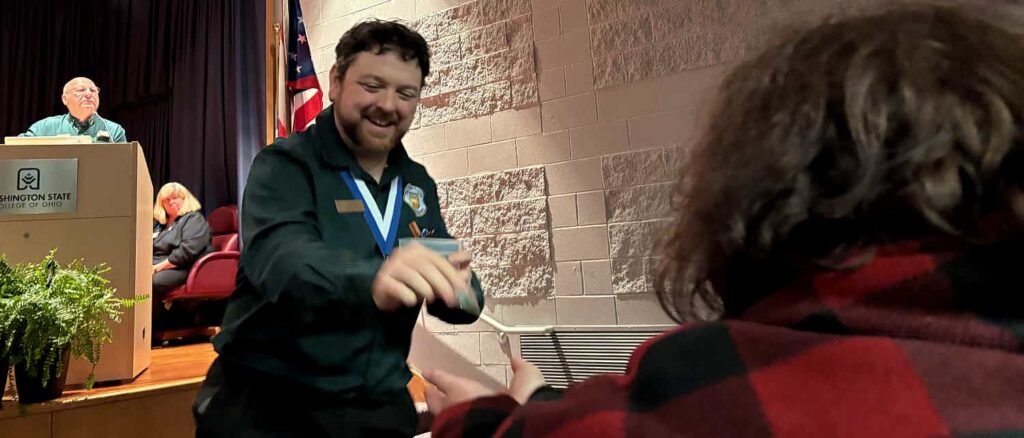 Advisor David Sigmund watching over Beta Gamma Epsilon Chapter President as they hand the Chapter Webmaster an Employment Edge pin.