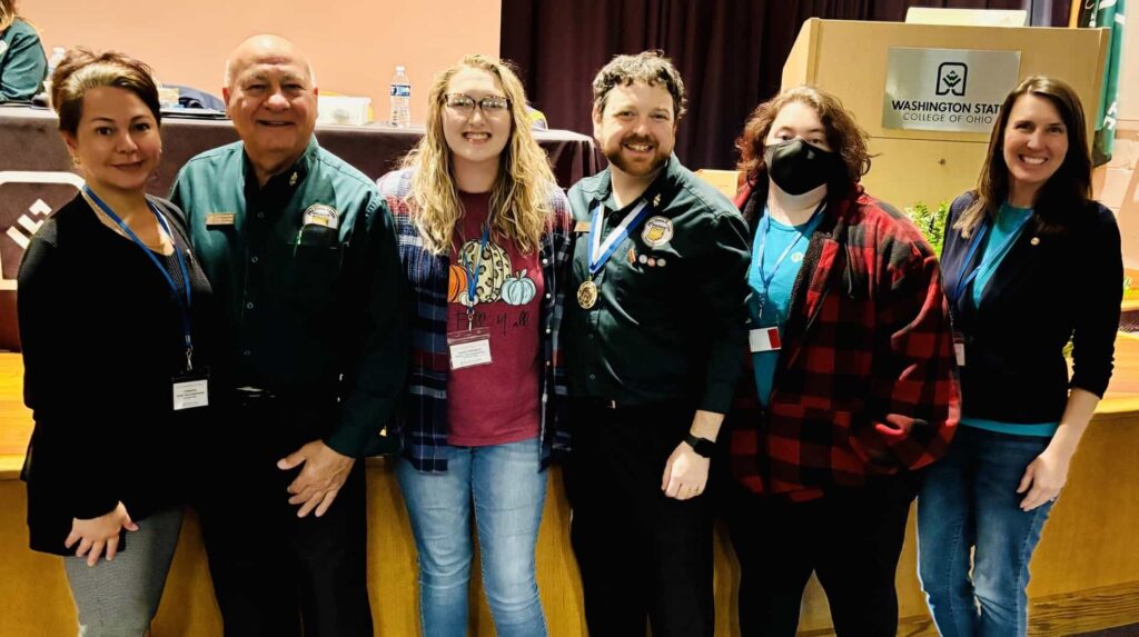 6 Phi Theta Kappans involved with the Beta Gamma Epsilon chapter standing in front of the conference stage.